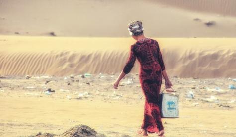 Woman in a national costume walking by the shore carrying a bucket of water