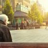 Rear view of older man sitting on a bench in a city